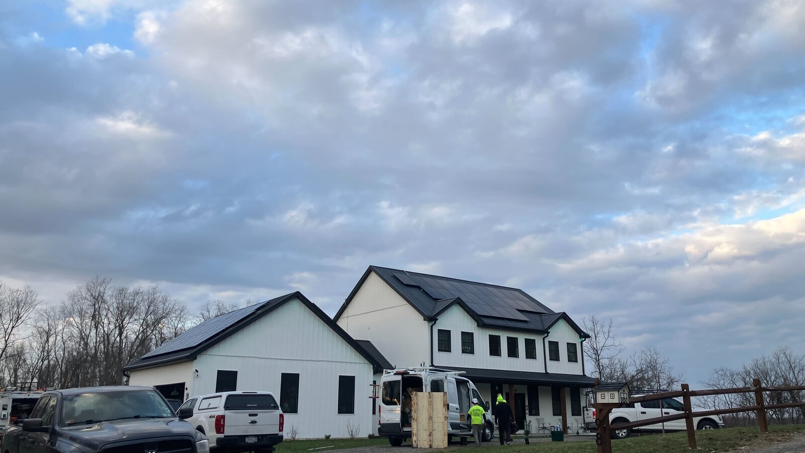 Modern white farmhouse with rooftop solar panels at dusk, with Lifestyle Solar work vehicles in the driveway